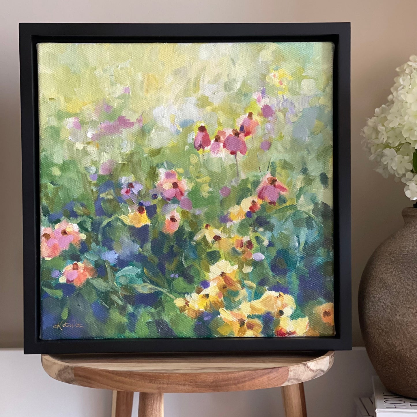 Framed painting of a floral scene on a wooden stand with a vase in the background.